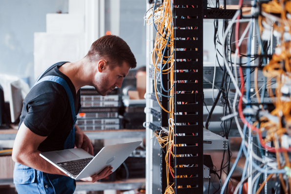 Image of a man working with cables and holding onto his laptop while he inspects them