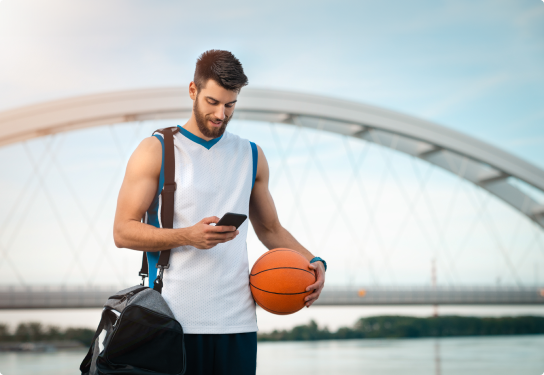 Image of a man texting on a mobile phone while holding a basketball in sports gear