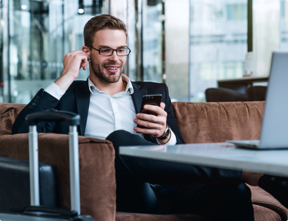 Man sitting  on a sofa adjusting his airpod in his ear while looking at his mobile phone