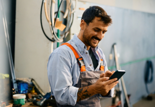 Photo of a man in work overalls smiling at his mobile phone