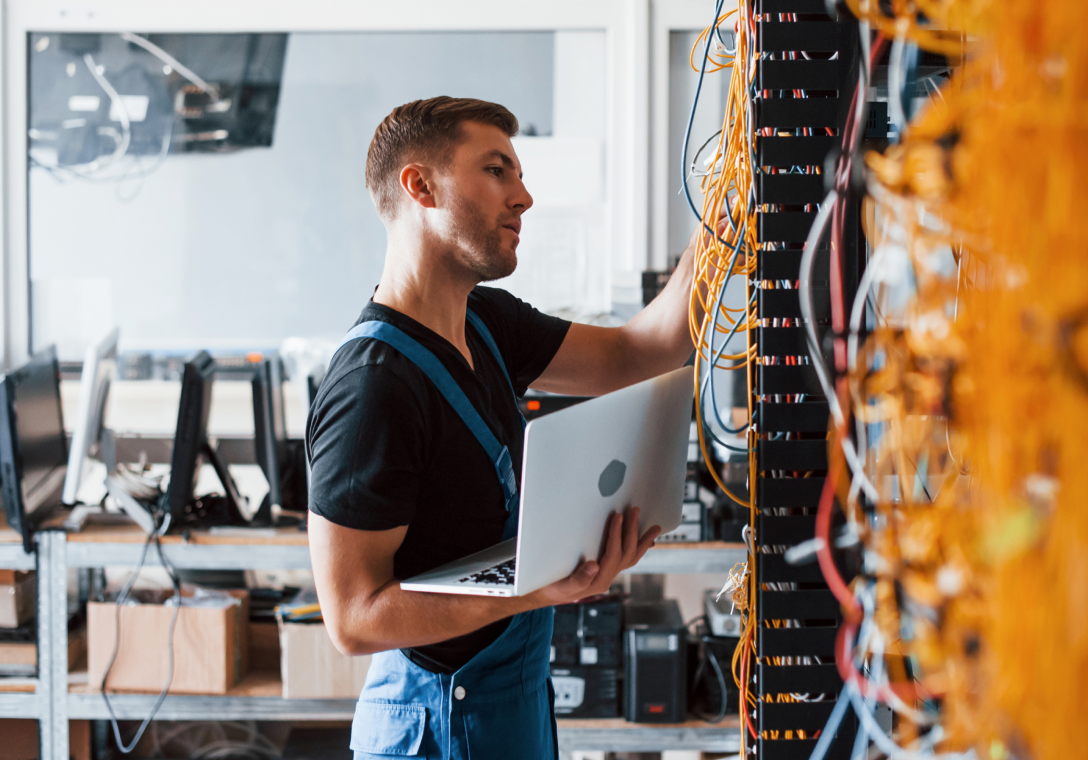 Image of a man working with cables and holding onto his laptop while he inspects them