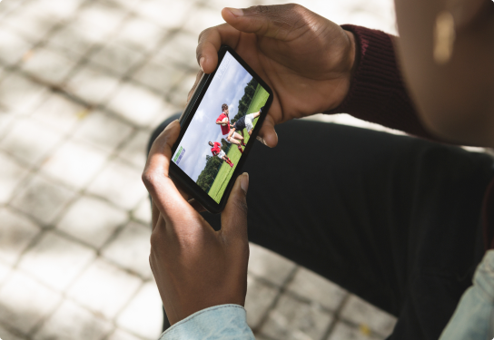 Image of a man holding a mobile phone watching a rugby game on the screen