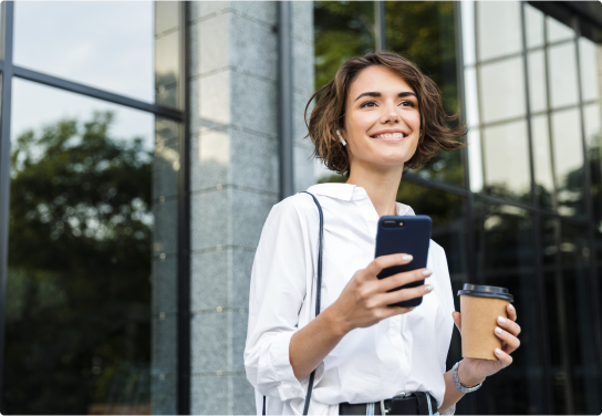 Woman outside a office building holding a mobile phone and a coffee