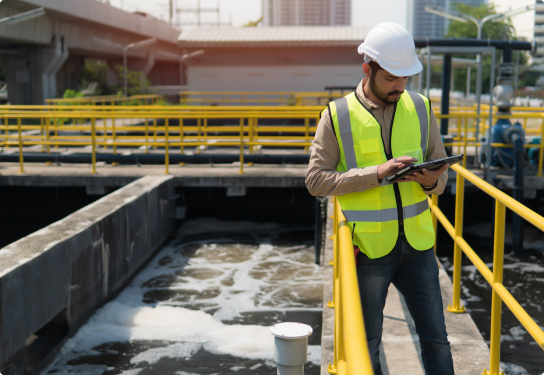 Image of a worker in a hard hat and high visibility vest using a tablet on a bridge over water