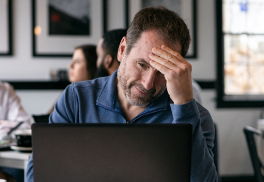 Image of a man working on his laptop scratching his head