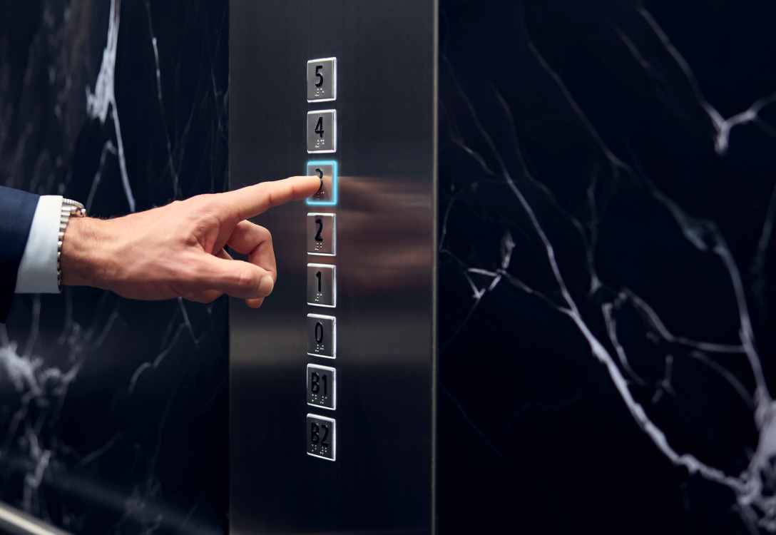 Phot of a person in a suit pressing an elevator button to get to the third floor