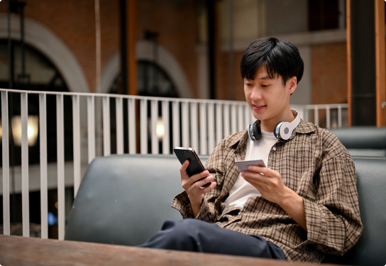 Image of a student sitting at a table on his mobile phone entering credit card details