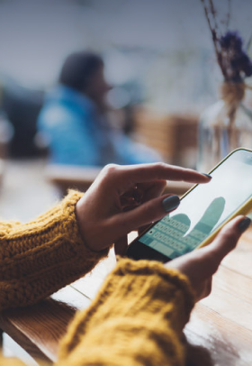 over the shoulder shot of a woman in a sweater using her smartphone in a cafe