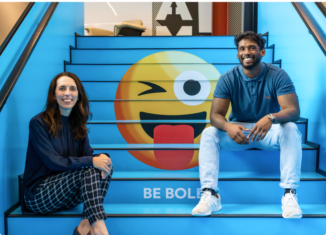 Photo of two 2degrees workers sitting on the staircase in the Auckland office with the Be Bold emoji painted on the stairs