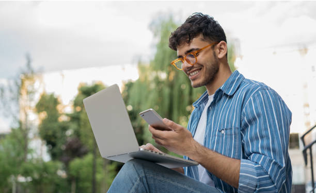Man sitting outside working on his laptop and looking at his mobile phone