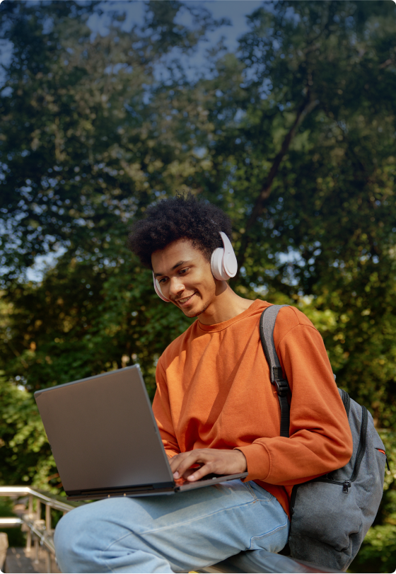 Image of a boy on his laptop wearing headphones sitting outside