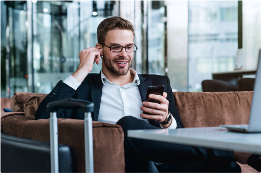 Man sitting  on a sofa adjusting his airpod in his ear while looking at his mobile phone