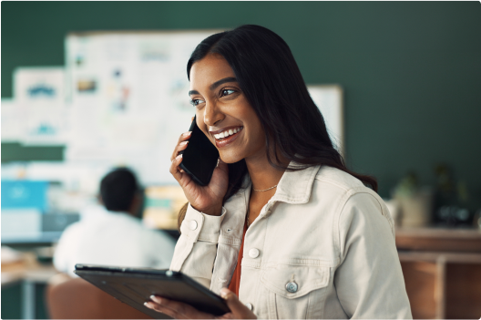 Photo of a woman on a mobile phone call while holding a tablet in the other hand