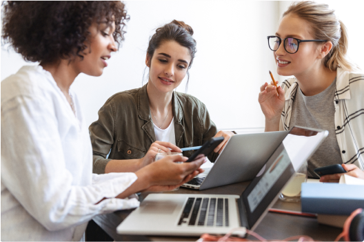 Three woman working around a table on laptops and a mobile phone