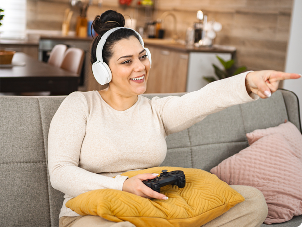 Girl sitting on the couch playing video games and wearing headphones pointing at something out of view
