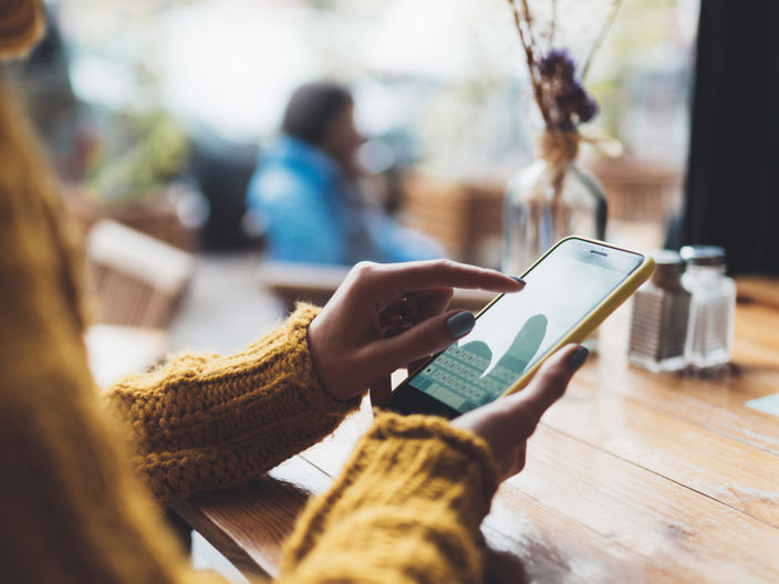 over the shoulder shot of a woman in a sweater using her smartphone in a cafe