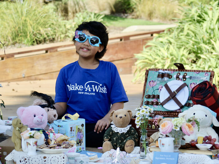 Photo of a child in a make-a-wish New Zealand t-shirt surrounded by toys 